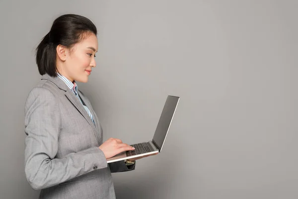 Side View Smiling Young Businesswoman Suit Using Laptop Grey Background — Stock Photo, Image