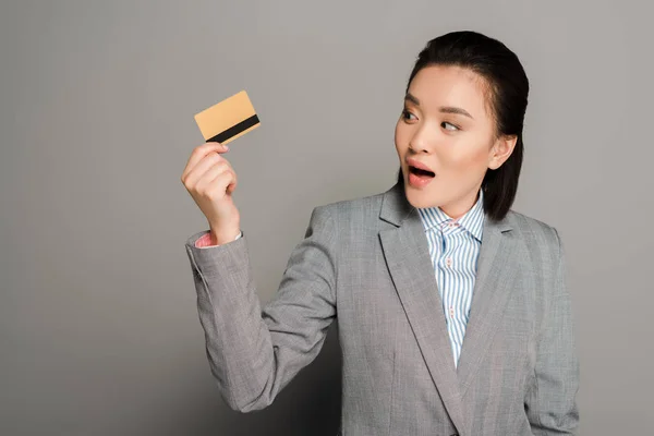Zszokowana Młoda Bizneswoman Garniturze Posiadająca Kartę Kredytową Szarym Tle — Zdjęcie stockowe