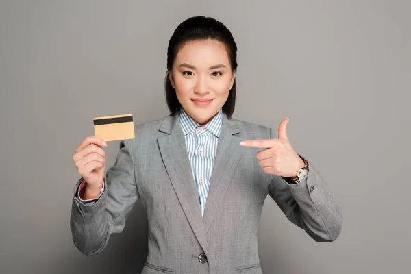 Sonriente Joven Mujer Negocios Traje Apuntando Tarjeta Crédito Sobre Fondo — Foto de Stock