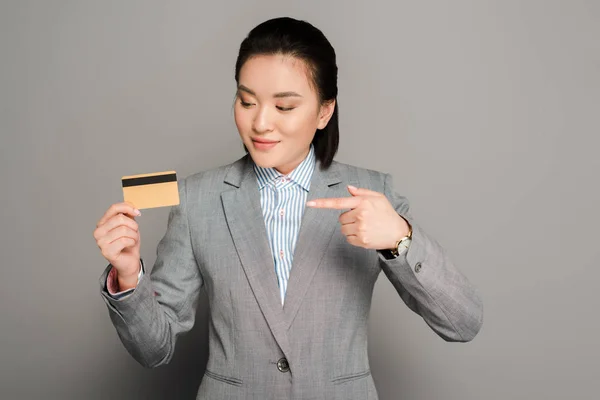 Усміхнена Молода Бізнес Леді Костюмі Вказуючи Кредитну Картку Сірому Фоні — стокове фото