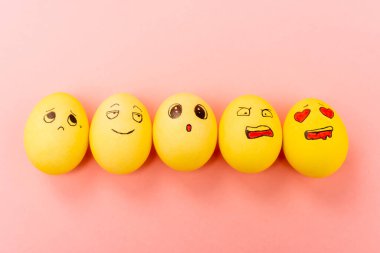 Top view of painted Easter eggs with different facial expressions on pink background clipart