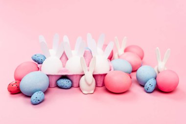 Renkli paskalya yumurtalı yumurta tepsisi ve pembe arka planda dekoratif tavşanlar.
