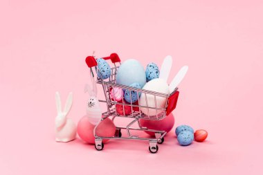 Renkli paskalya yumurtaları ve pembe arka planda süslü tavşanlar.