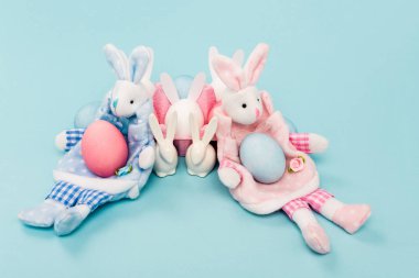 Boyalı tavuk yumurtaları ve mavi arka planda dekoratif paskalya tavşanları.