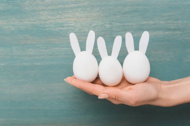Ahşap arka planda dekoratif paskalya tavşanları olan kadın eli.