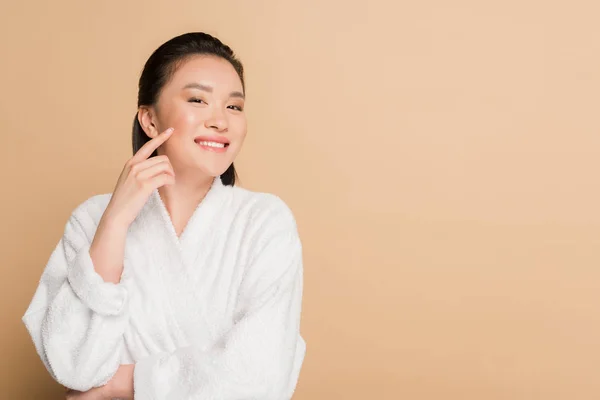 笑顔美しいアジア人女性でバスローブで顔に触れる上のベージュの背景 — ストック写真