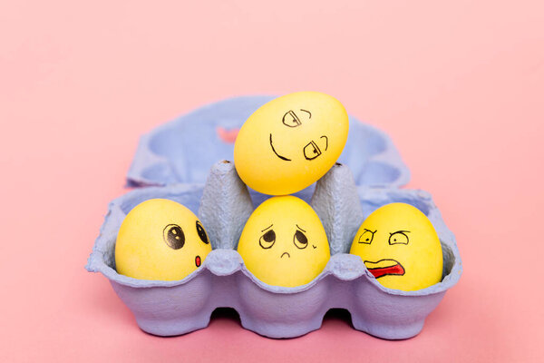 Selective focus of easter eggs with facial expressions in egg tray on pink 