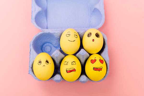 Top view of colorful easter eggs with facial expressions in egg tray on pink background