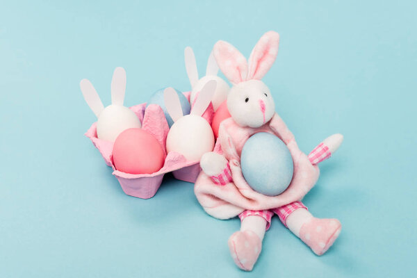 Pink egg tray with painted chicken eggs and decorative bunnies on blue, easter concept