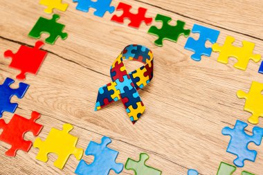 High angle view of awareness ribbon with pieces of puzzle on wooden background, autism concept clipart