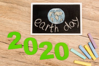 Tahtada dünya günü harfleri, 2020 haneli rakamlar ve tahta zemin üzerindeki tebeşir parçaları var.