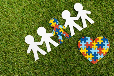 Top view of special kid with autism among another and decorative heart on green background clipart