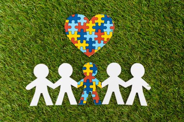 Top view of special kid with autism among another and decorative puzzle heart on green clipart