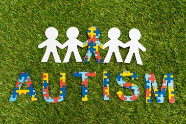 Top view of autism puzzle lettering and special kid among another on green background clipart