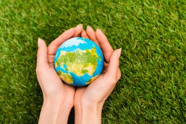 Cropped view of globe in female hands on green background, earth day concept clipart