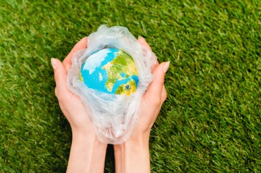 Cropped view of plastic bag with globe in female hands on green, global warming concept clipart