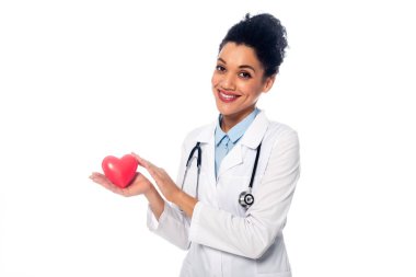 Steteskopla gülümseyen ve dekoratif kırmızı kalp gösteren Afrikalı Amerikalı doktor beyaza izole edilmiş.