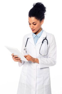 Beyazlar üzerinde izole edilmiş dijital tablet kullanan, steteskoplu Afrikalı Amerikalı doktorun ön görüntüsü.