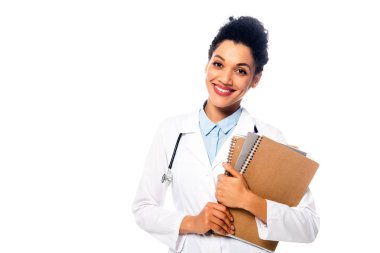 Steteskop, not defteri ve klasörü beyaz üzerine izole edilmiş gülümseyen Afrikalı Amerikalı doktorun ön görüntüsü.