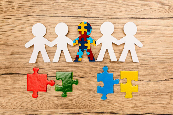 Вид сверху на особенного ребенка с аутизмом среди других с разноцветными кусочками пупса на деревянном фоне
