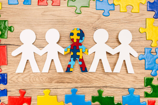 Top view of bright pieces of puzzle and special kid with autism among another on wooden background
