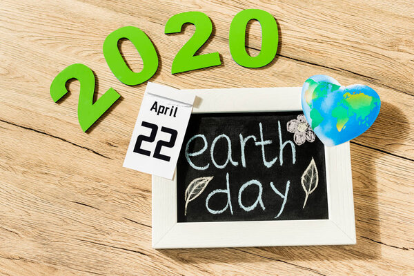High angle view of board with earth day lettering, calendar with 22 april 2020 inscription and globe on wooden background