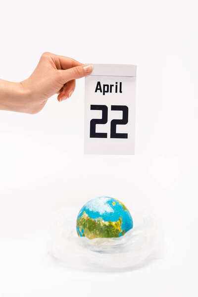Cropped view of woman holding calendar with 22 april inscription and globe in plastic bag on white background, global warming concept