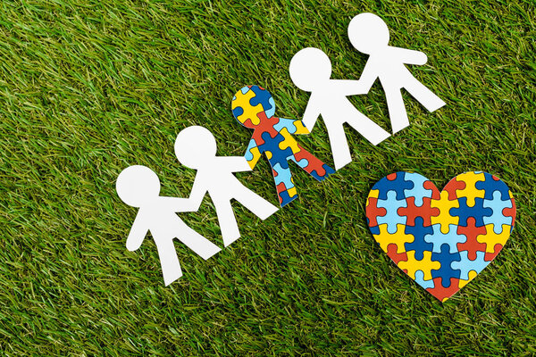 Top view of special kid with autism among another and decorative heart on green background