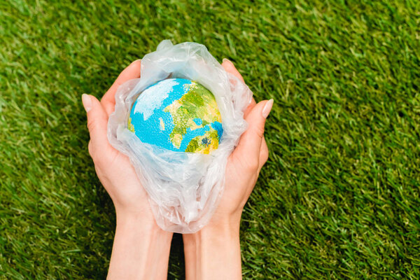 Cropped view of plastic bag with globe in female hands on green, global warming concept