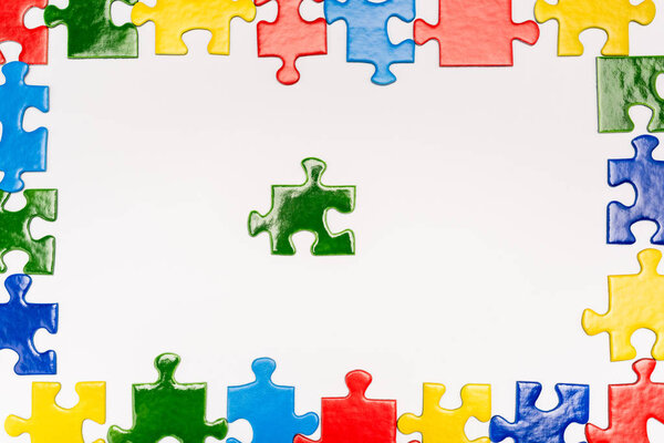Top view of frame with bright pieces of puzzle on white background, autism concept