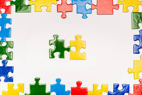 Top view of frame with multicolored pieces of puzzle on white background, autism concept