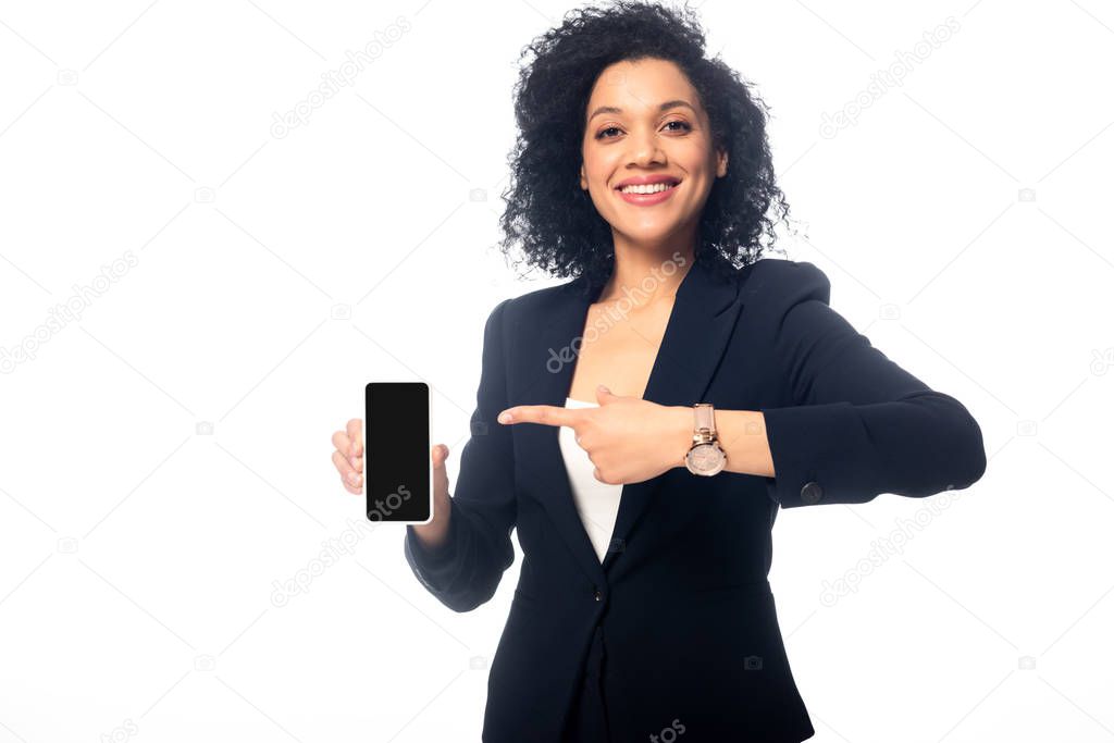 Front view of african american woman pointing at smartphone, smiling and looking at camera isolated on white