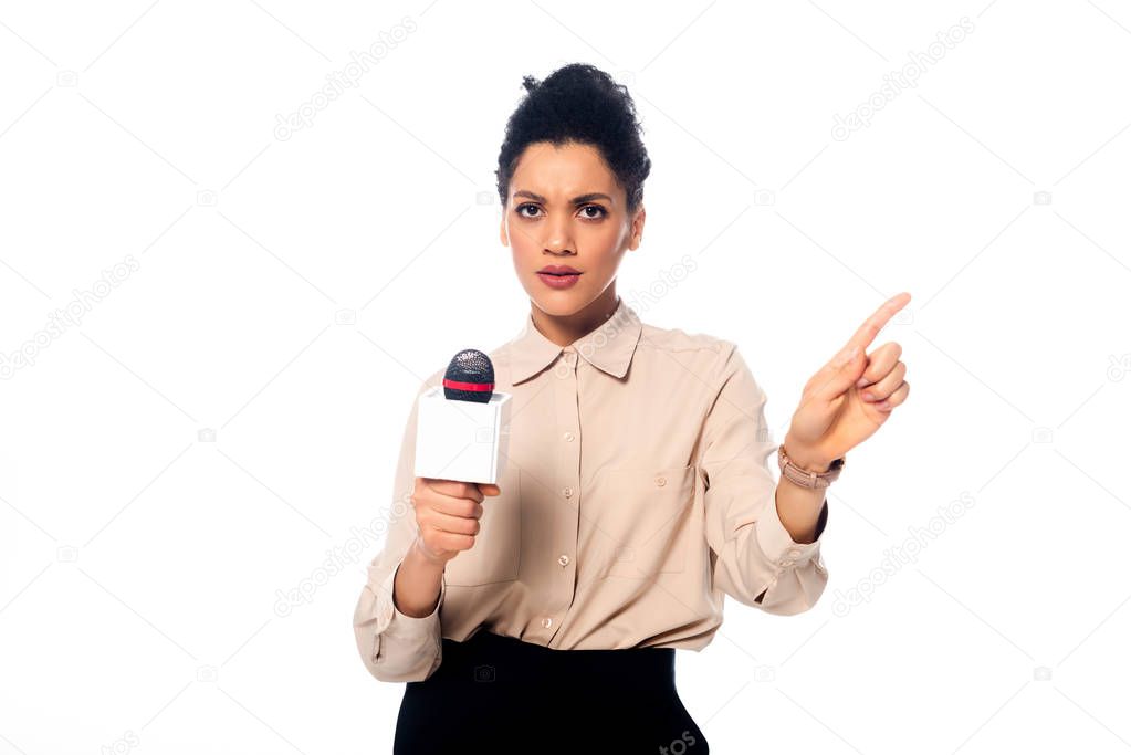 African american journalist with microphone looking at camera and pointing with finger aside isolated on white