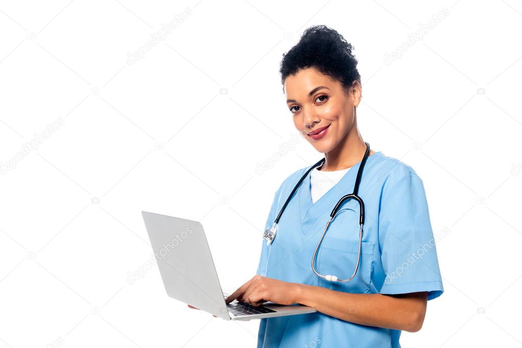 African american nurse with stethoscope and laptop smiling and looking at camera isolated on white