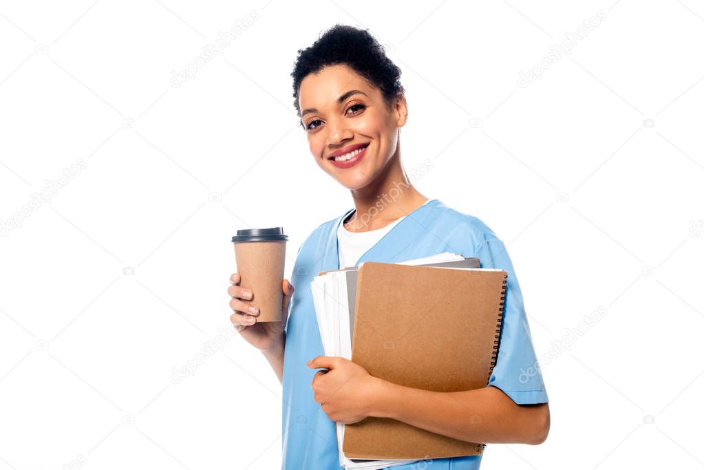 Happy and positive african american nurse with papers and disposable cup of coffee looking at camera isolated on white