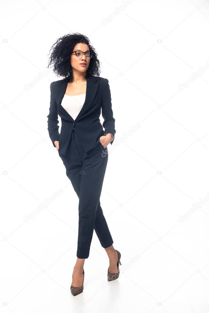Full length view of confident african american businesswoman walking with hands in pockets on white background