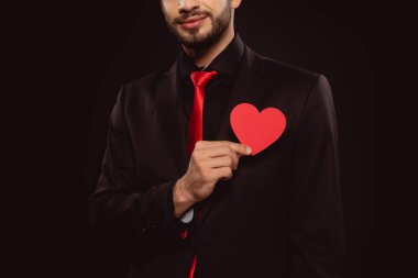 Kırpılmış görüntüde kırmızı kalp şeklinde kağıt tutan zarif bir adam siyah üzerine izole edilmiş.