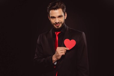 Elinde kağıt kalp tutan yakışıklı bir adam ve siyah bir kameraya bakıyor.