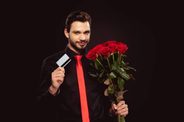 Siyah kameraya bakarken elinde kredi kartı ve güller tutan yakışıklı bir adam.
