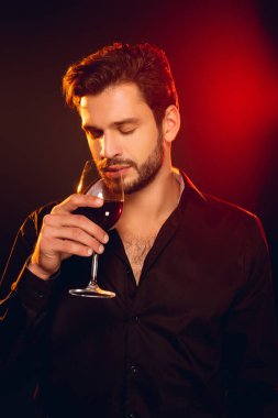 Yakışıklı adam siyah arka planda kırmızı şarap içiyor.