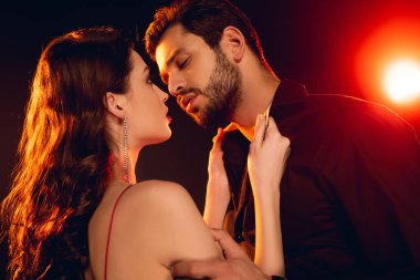 Siyah arka planda erkek arkadaşının düğmelerini açan güzel bir kadının yan görüntüsü.