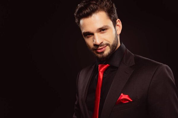 Handsome man in formal wear and red tie looking at camera isolated on black