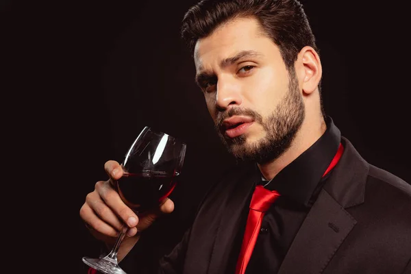 穿着正装 打着红领带的英俊男人拿着用黑色隔开的红酒 看着相机 — 图库照片