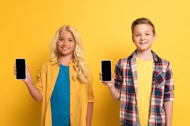 Sarı arka planda kopya alanı olan akıllı telefonları tutan gülümseyen çocuklar  