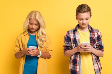 Gülümseyen ve tatlı çocuklar sarı arka planda akıllı telefon kullanıyorlar. 