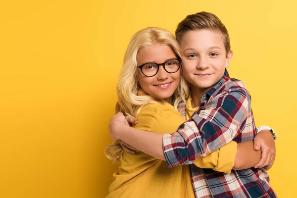 Uśmiechnięte Dzieci Przytulające Się Patrzące Kamerę Żółtym Tle — Zdjęcie stockowe