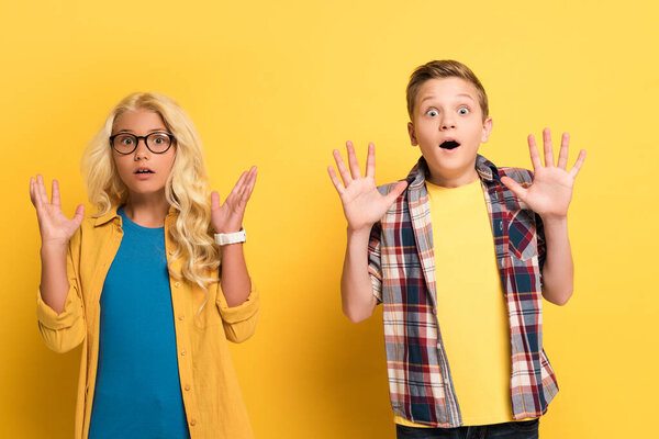 shocked kids with outstretched hands looking at camera on yellow background 