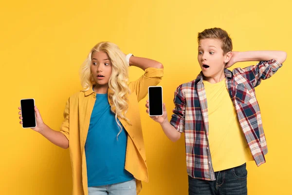 Şaşırmış Çocuklar Ellerinde Sarı Arkaplanda Kopya Alanı Olan Akıllı Telefonlar — Stok fotoğraf