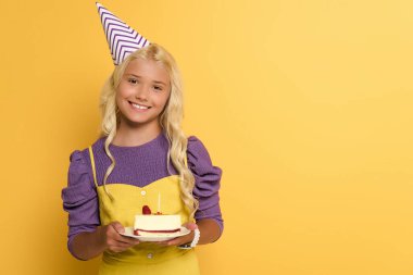 Sarı arka planda doğum günü pastası olan gülümseyen çocuk. 