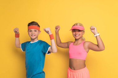 Spor kıyafetli gülümseyen çocuklar sarı arka planda güçlü bir hareket sergiliyorlar. 